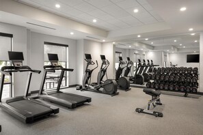 Une salle de sport équipée de tapis de course, de vélos elliptiques et d’une série de haltères.