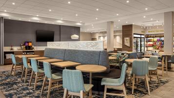 A modern hotel lobby with seating areas, a television, and a snack bar.