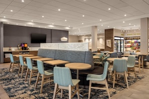 A modern hotel lobby with seating areas, a television, and a snack bar. - Home2 Suites By Hilton Salisbury Fruitland (Fruitland)