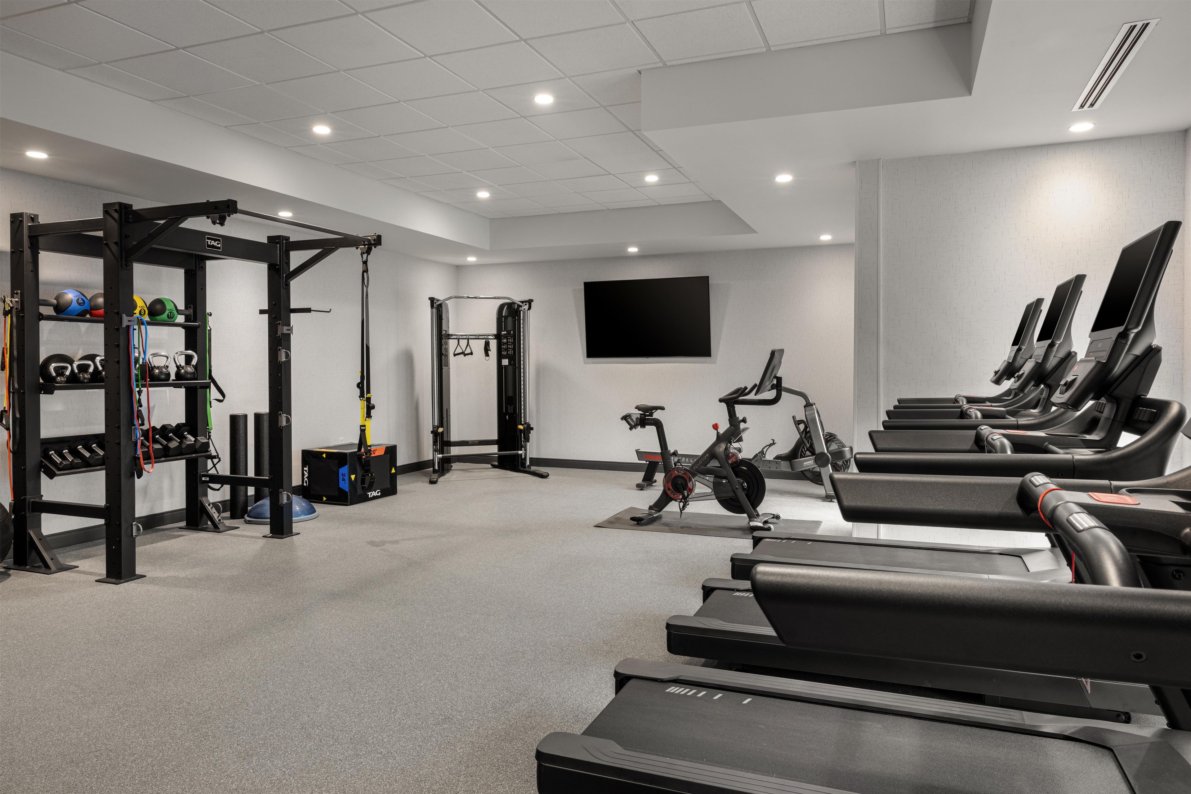 A gym with treadmills, weightlifting equipment, and a TV screen.