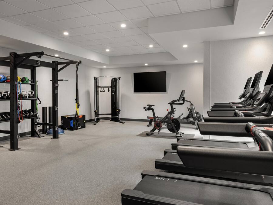 A gym with treadmills, weightlifting equipment, and a TV screen.