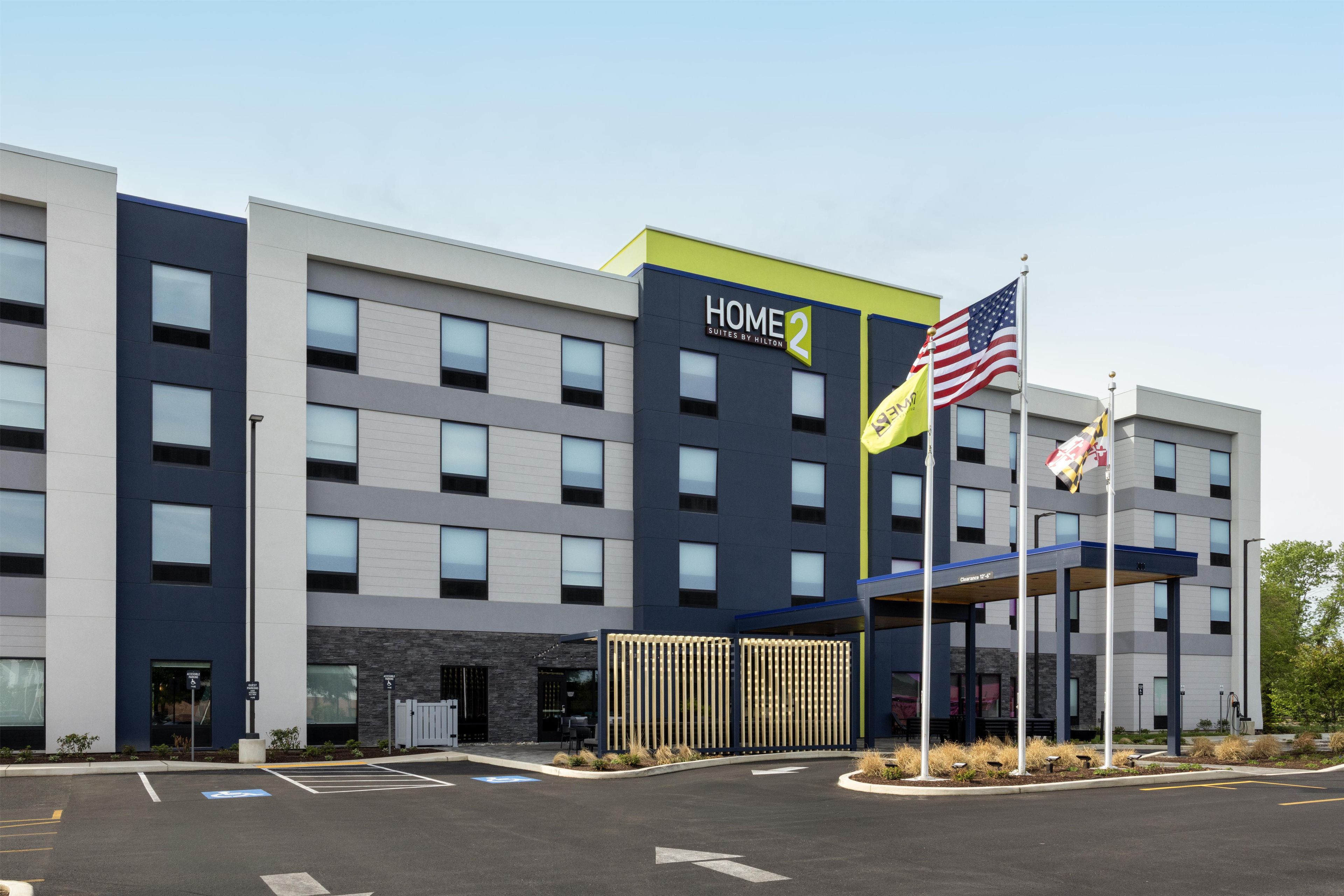 Un edificio moderno de hotel con un letrero 'HOME 2', varias banderas y un acceso cubierto.