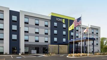 A modern hotel building with a 'HOME 2' sign, multiple flags, and a covered entrance.