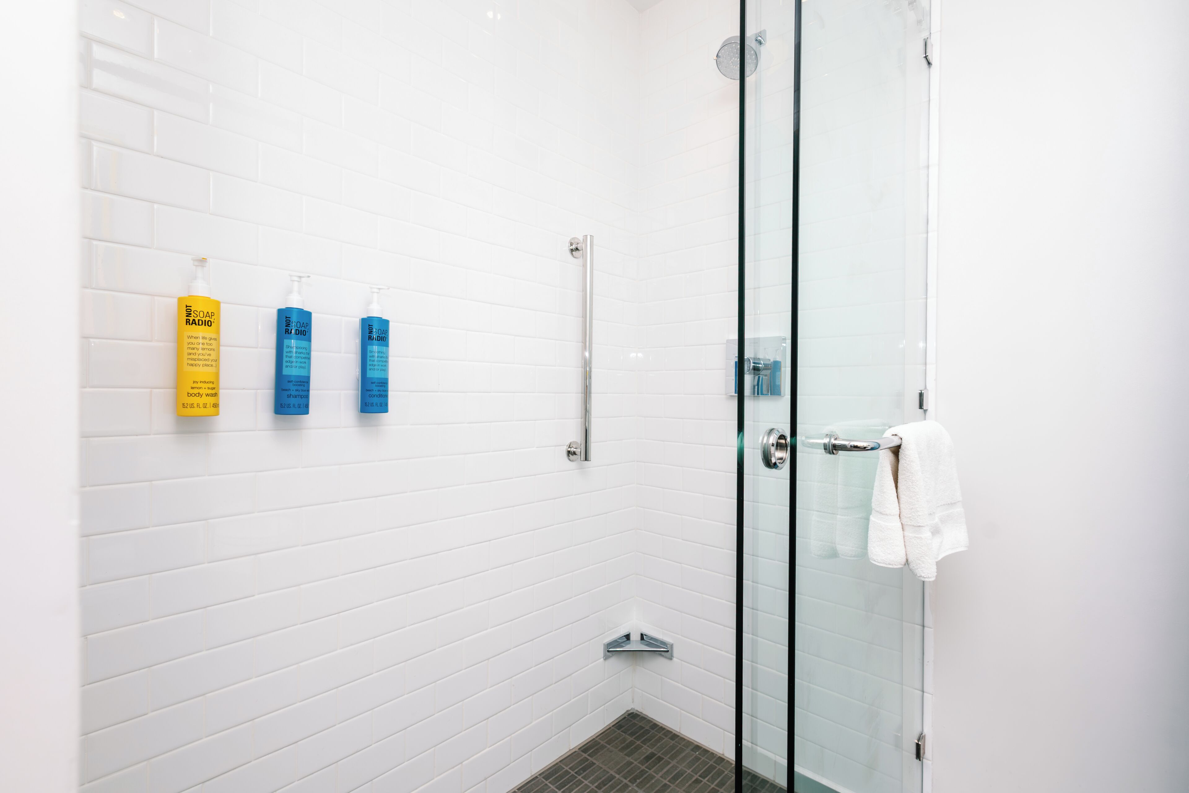 A modern bathroom with white subway tiles, a glass shower enclosure, and three toiletries on the wall.