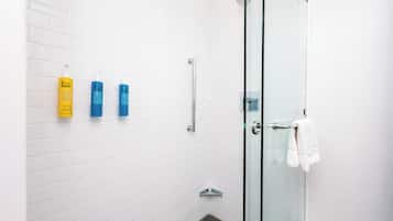 A modern bathroom with white subway tiles, a glass shower enclosure, and three toiletries on the wall.