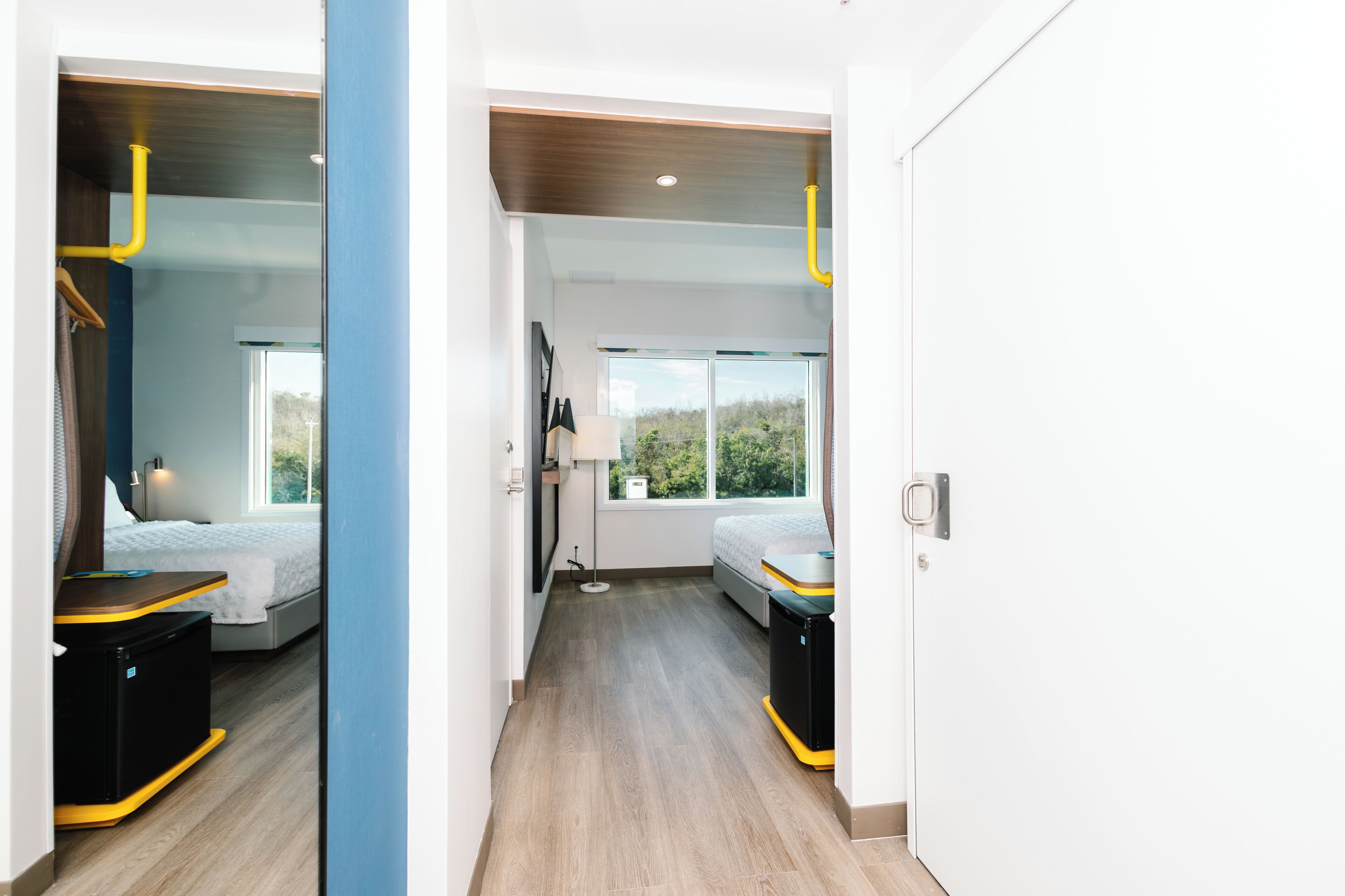 Habitación de hotel moderna con cama, mesita de noche, lámpara y vistas al exterior a través de amplias ventanas.