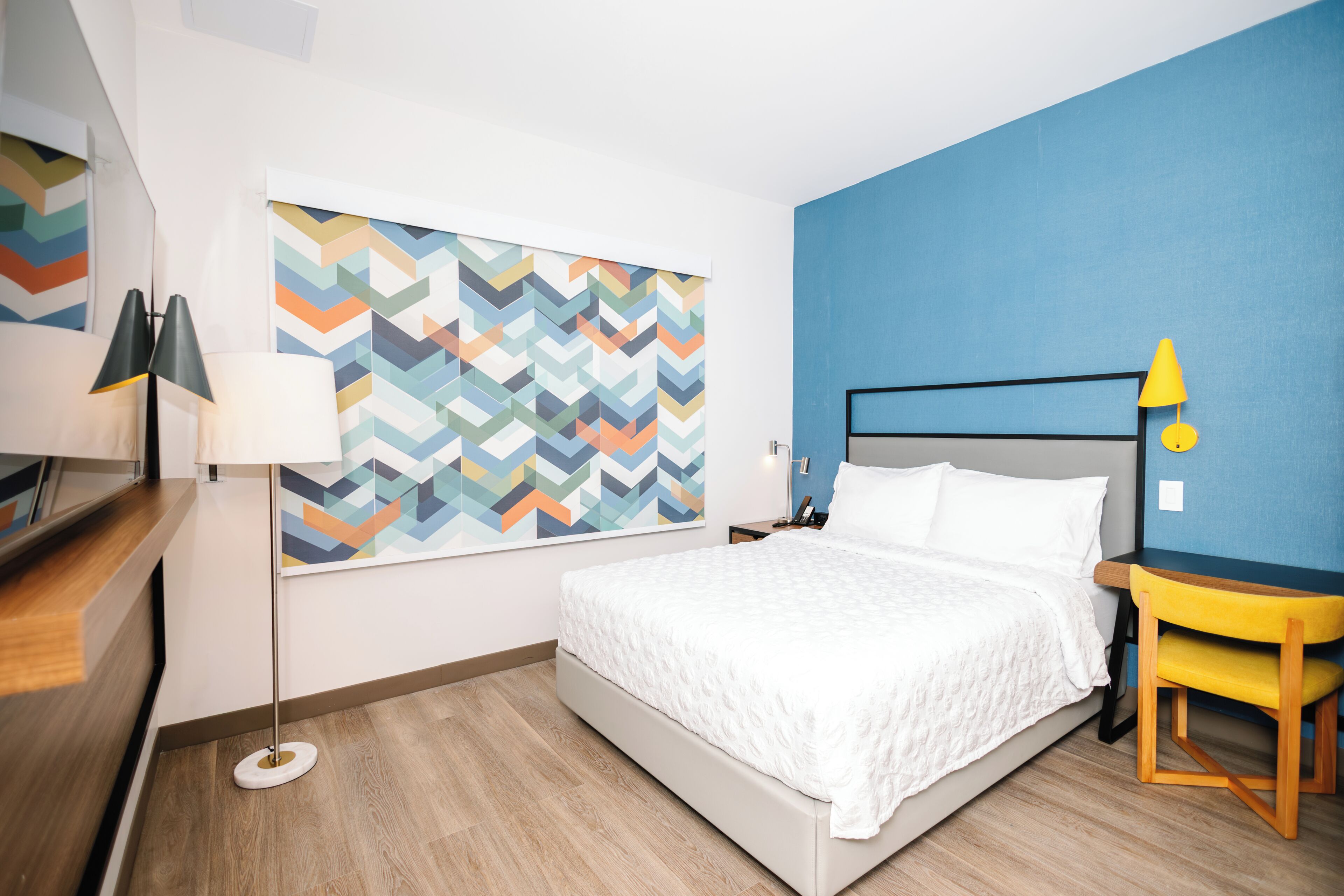 Une chambre d’hôtel avec un lit, une table de chevet, une lampe et un mur orné d’un motif géométrique.