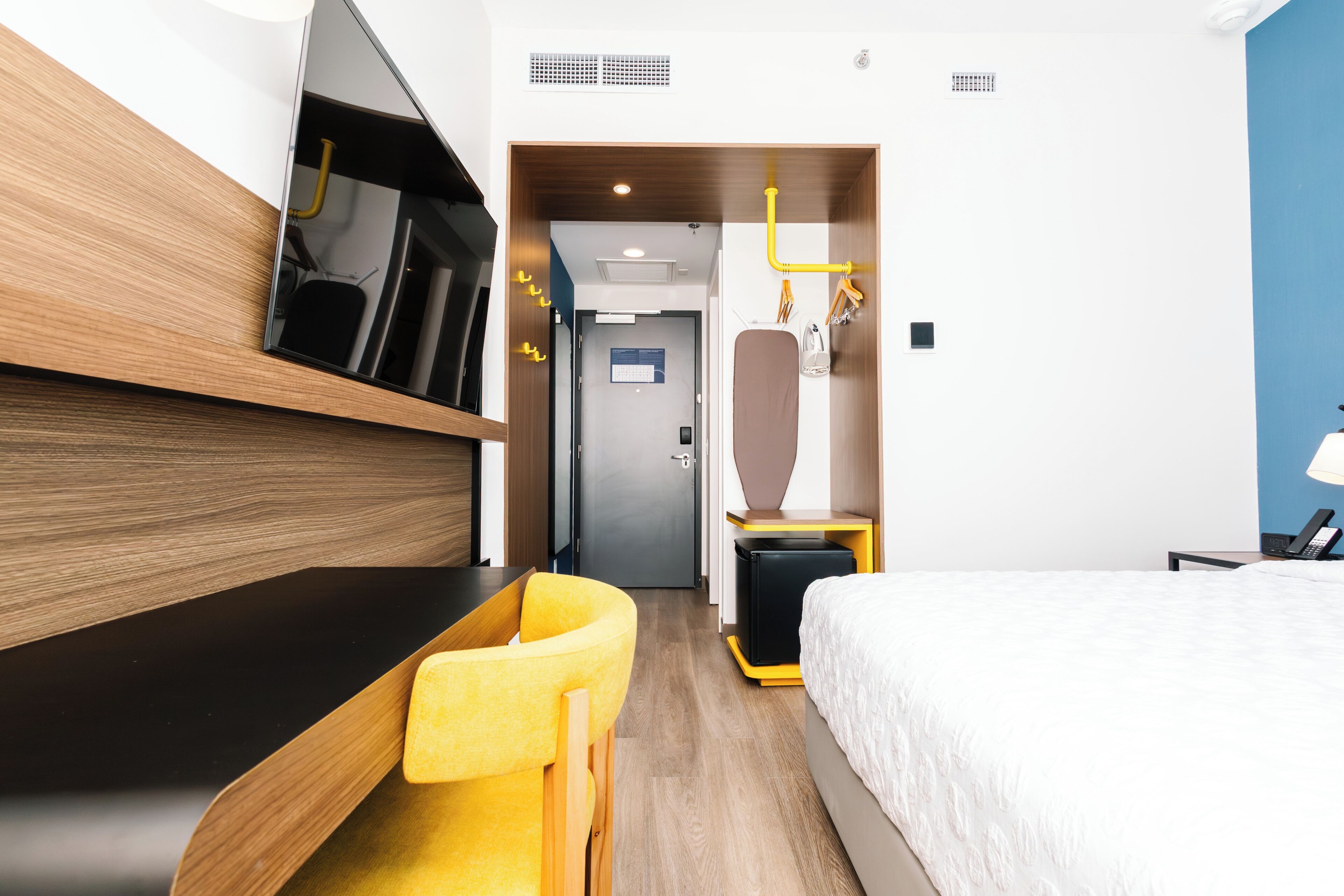 A hotel room with a bed, a desk with a chair, a television, a wardrobe, and a bathroom with a mirror.