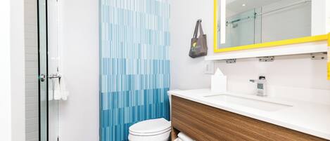 Un baño moderno con inodoro blanco, tocador de madera y cortina de ducha estampada en azul.