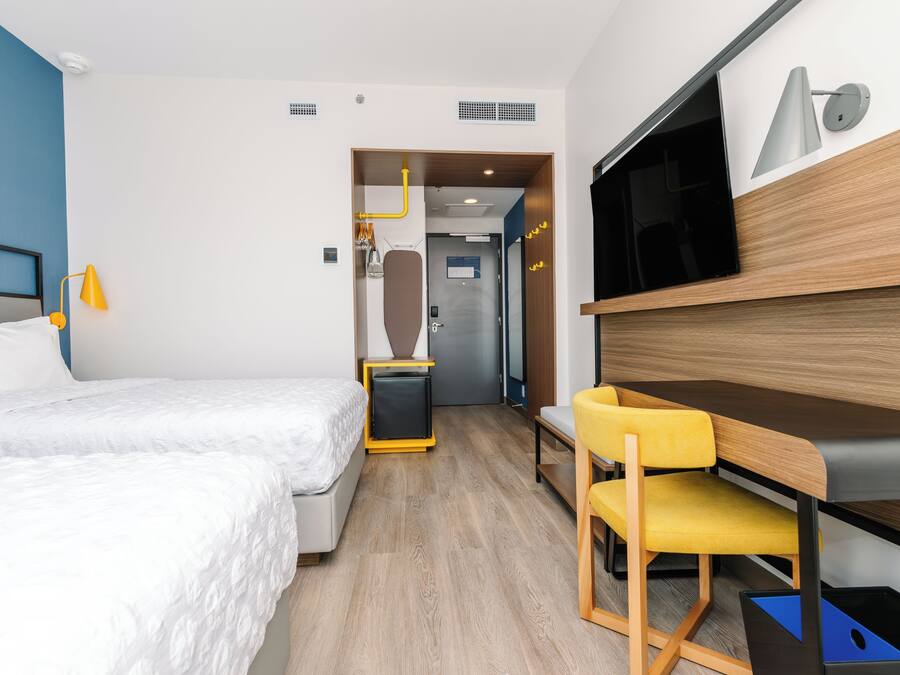 A hotel room with a bed, a desk with a chair, a TV, and a wardrobe.