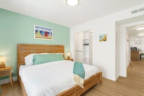 A bedroom with a wooden bed, a nightstand, a wall-mounted shelf, and a door leading to a bathroom.