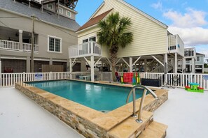 A swimming pool with a stone border, a palm tree, and a white fence.