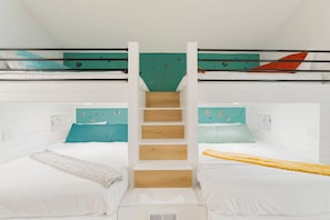 Une chambre avec un lit superposé, une échelle en bois au centre, des murs blancs et des œuvres d’art colorées.