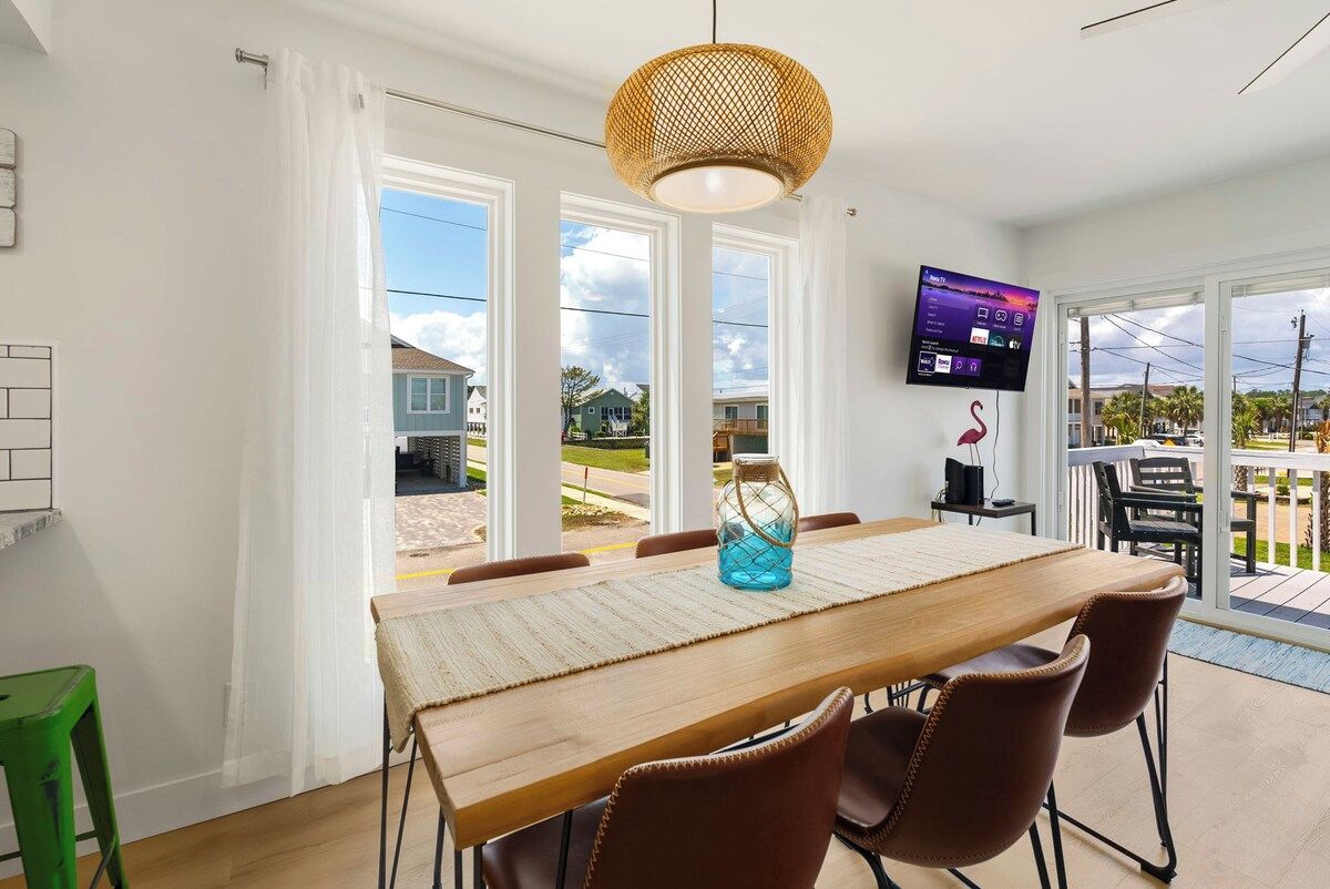 A dining area with a wooden table, brown chairs, a woven pendant light, and a TV on the wall.