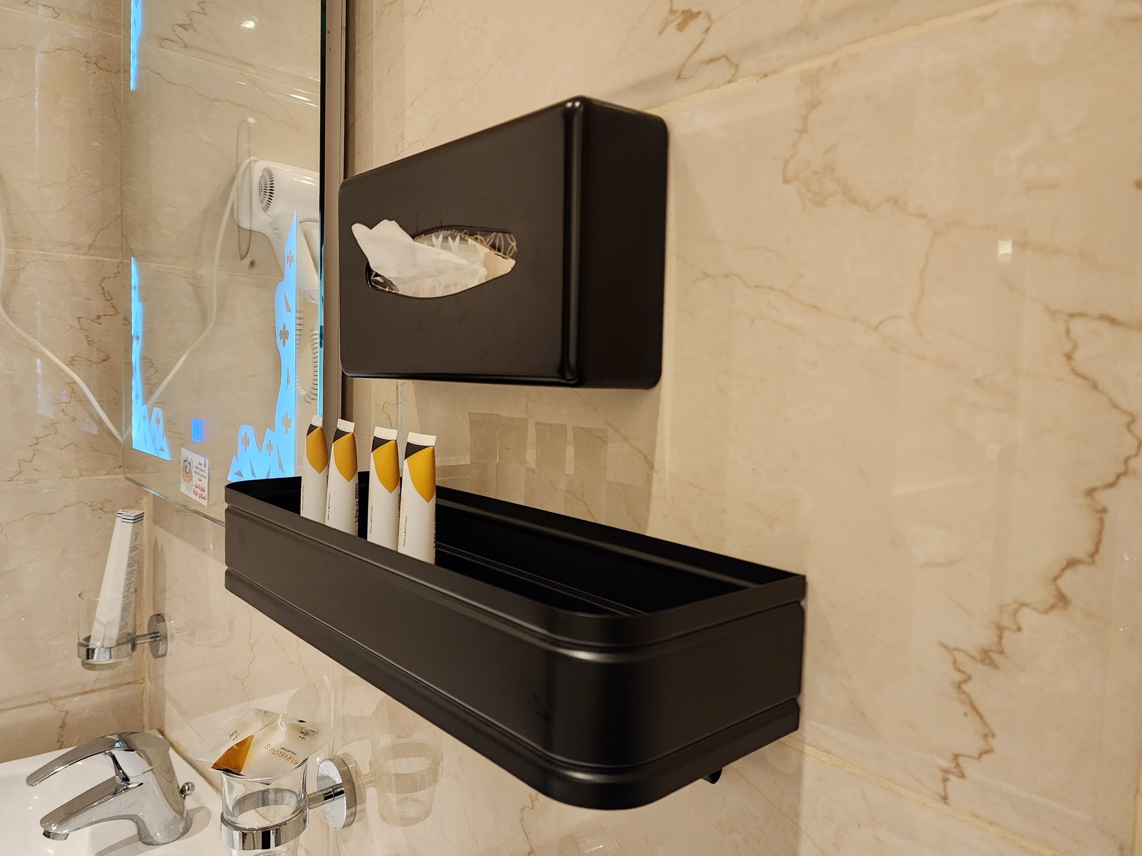 Une salle de bain avec un porte-savon noir, un miroir et un mur en marbre.