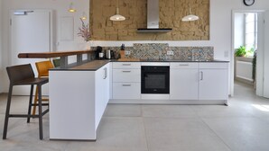 A modern kitchen with white cabinetry, a central island, pendant lighting, and a stone accent wall.