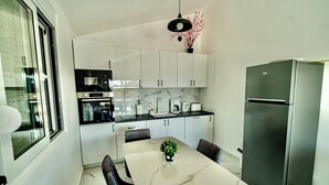 Una cocina moderna con armarios blancos, encimera de mármol, refrigerador de acero inoxidable y una mesa de comedor con sillas.