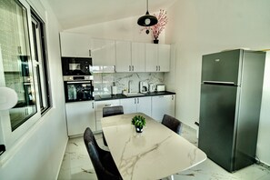 Une cuisine moderne avec des meubles blancs, un plan de travail en marbre, un réfrigérateur en acier inoxydable et une table à manger avec des chaises.