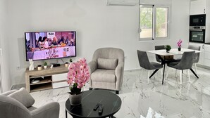 Una sala de estar moderna con televisor, sofá, mesa de comedor y zona de cocina.