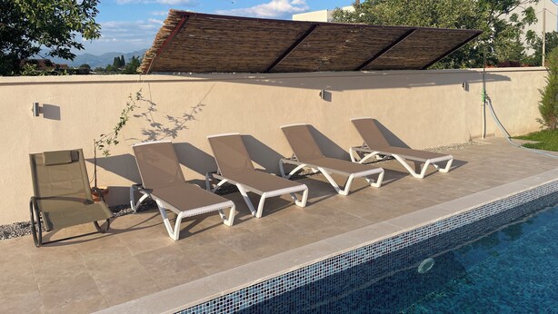 Un área junto a la piscina con sillones de descanso, una pérgola y vistas a las montañas.