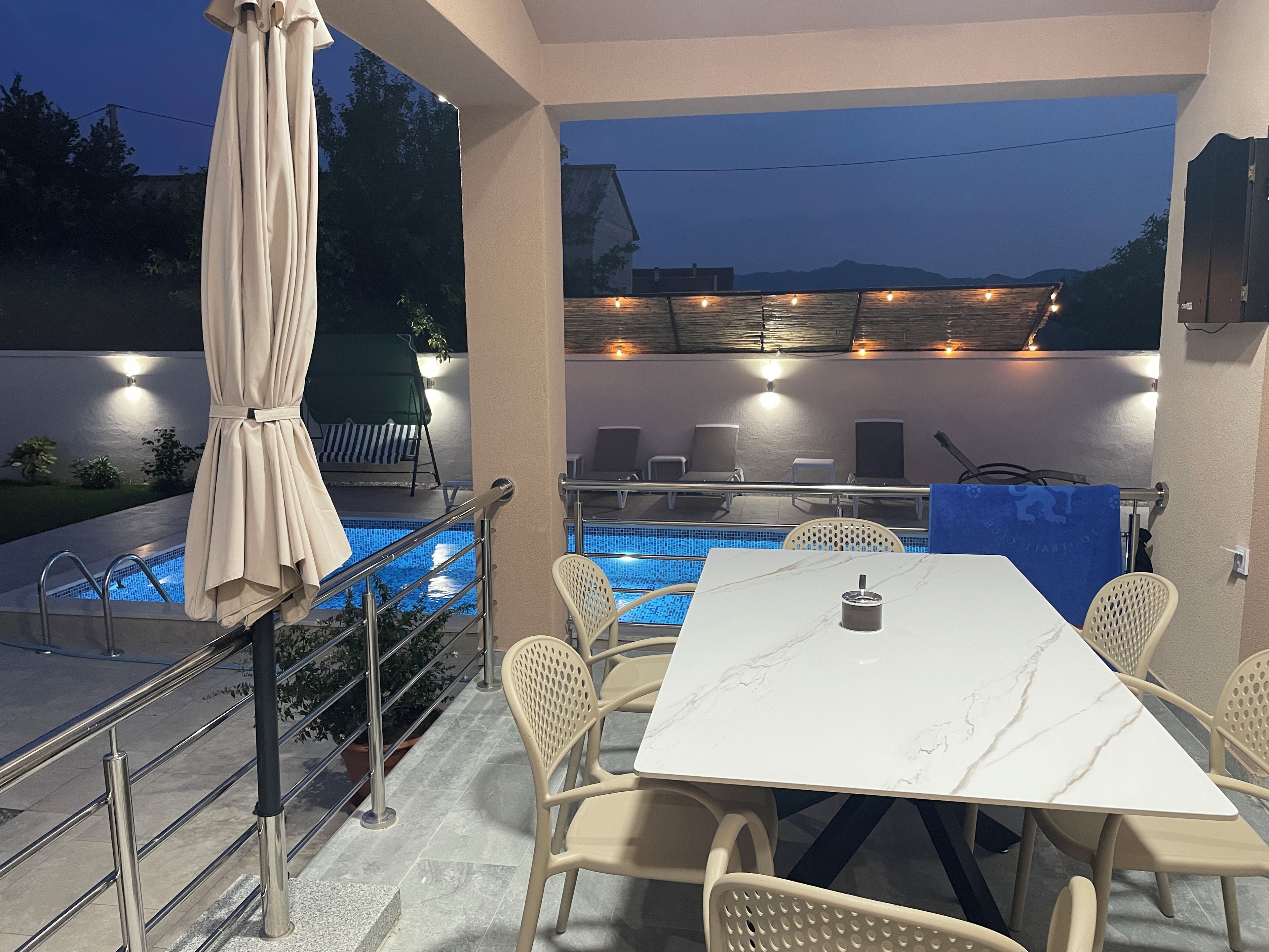 An outdoor pool area with a table and chairs, a covered seating area, and a view of the mountains.