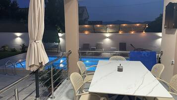An outdoor pool area with a table and chairs, a covered seating area, and a view of the mountains.