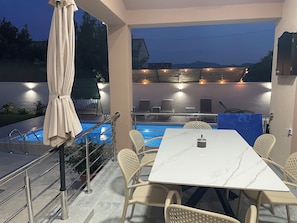 Zona de piscina exterior con mesa y sillas, un área de estar cubierta y vistas a las montañas.