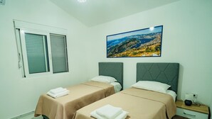 Una habitación de hotel con dos camas, una ventana con persianas, una mesita de noche con una lámpara y un cuadro de un paisaje.