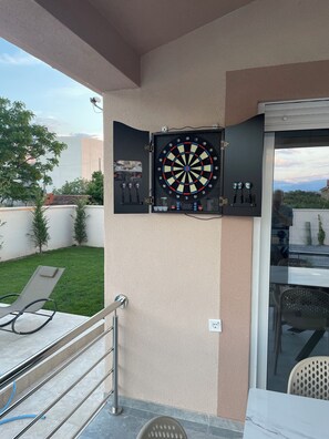 A dartboard mounted on a wall, a patio area with chairs, and a glass door leading outside. - 4: Peace and quiet between the sea and the mountains, in the countryside (Golubovci)