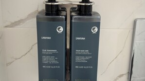 Dos botellas de productos capilares ANYAH, incluyendo acondicionador y champú, sujetas a la pared.