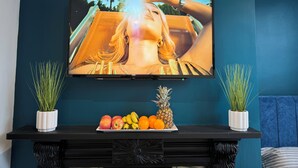 Un televisor montado en una pared azul verdoso, con una bandeja de frutas debajo.