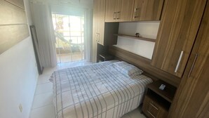 A bedroom with a bed, wooden wardrobe, and a sliding glass door leading to a balcony. - Your Refuge in Bombinhas – Airy family home close to the beach (Bombinhas)