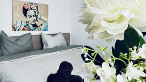 A bedroom with a bed, pillows, a painting on the wall, and a large white flower arrangement. - Bright and Spacious Room Near Kaufpark Alterlaa (Vienna)