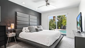 Ein modernes Schlafzimmer mit einem großen Bett, einem Deckenventilator, einem Fernseher und Blick auf einen Swimmingpool.