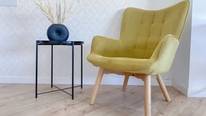A mustard yellow armchair with wooden legs and a black metal table beside it. - Plateia Suite Grigio (Nicosia)