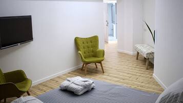 A bedroom with a bed, two green chairs, a flat-screen TV, and a wooden floor.