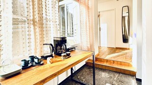 Une cuisine équipée d’une machine à café, de tasses et d’une fenêtre avec des rideaux.