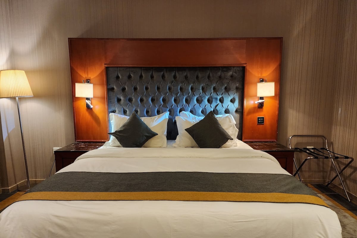A hotel room with a large bed, a tufted headboard, two bedside lamps, and a chair.