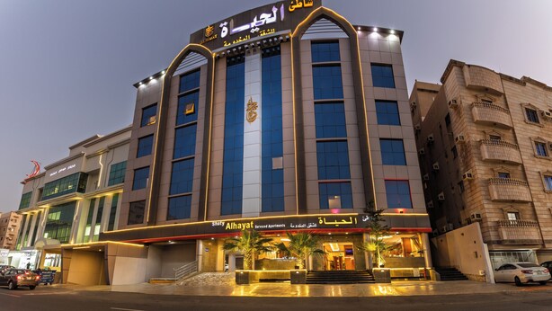 Een hotel met meerdere verdiepingen, een opvallende ingang, een groot bord met Arabische tekst en een modern architectuurontwerp.