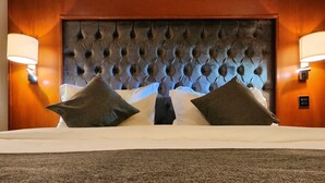 Een hotelkamer met een gestoffeerd hoofdeinde, twee kussens, een bed en twee wandlampen.