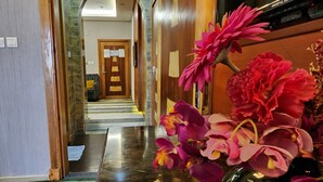 Een hotellobby met een marmeren vloer, een houten receptiebalie en een grote bloemenvaas.