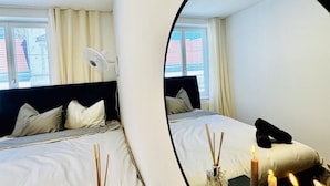Un dormitorio con cama, espejo, ventana y mesita de noche con velas.
