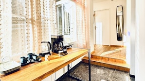 Una cocina con cafetera, tazas y una ventana con cortinas.