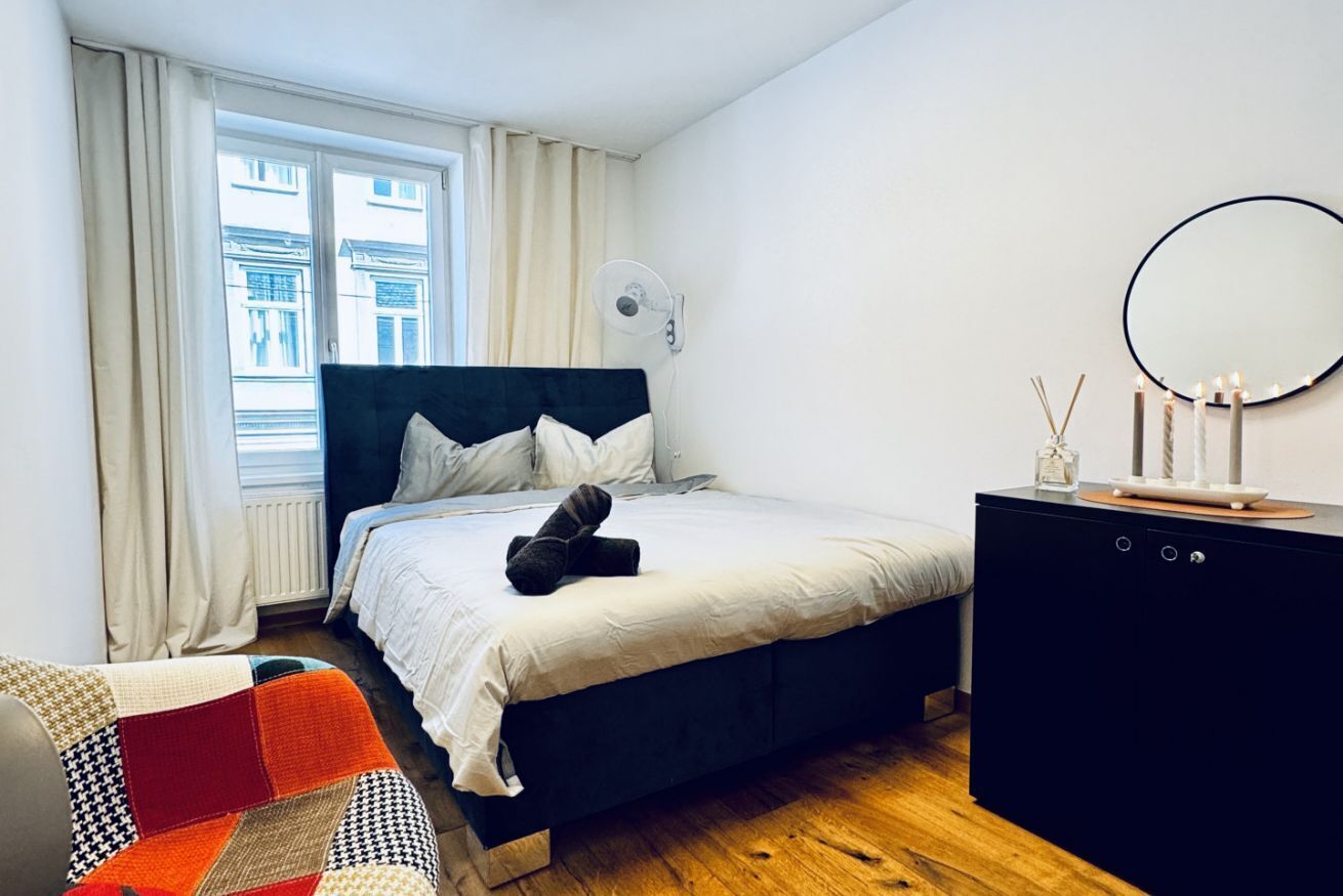 Une chambre à coucher avec un lit, une table de chevet, un miroir et une fenêtre avec des rideaux.