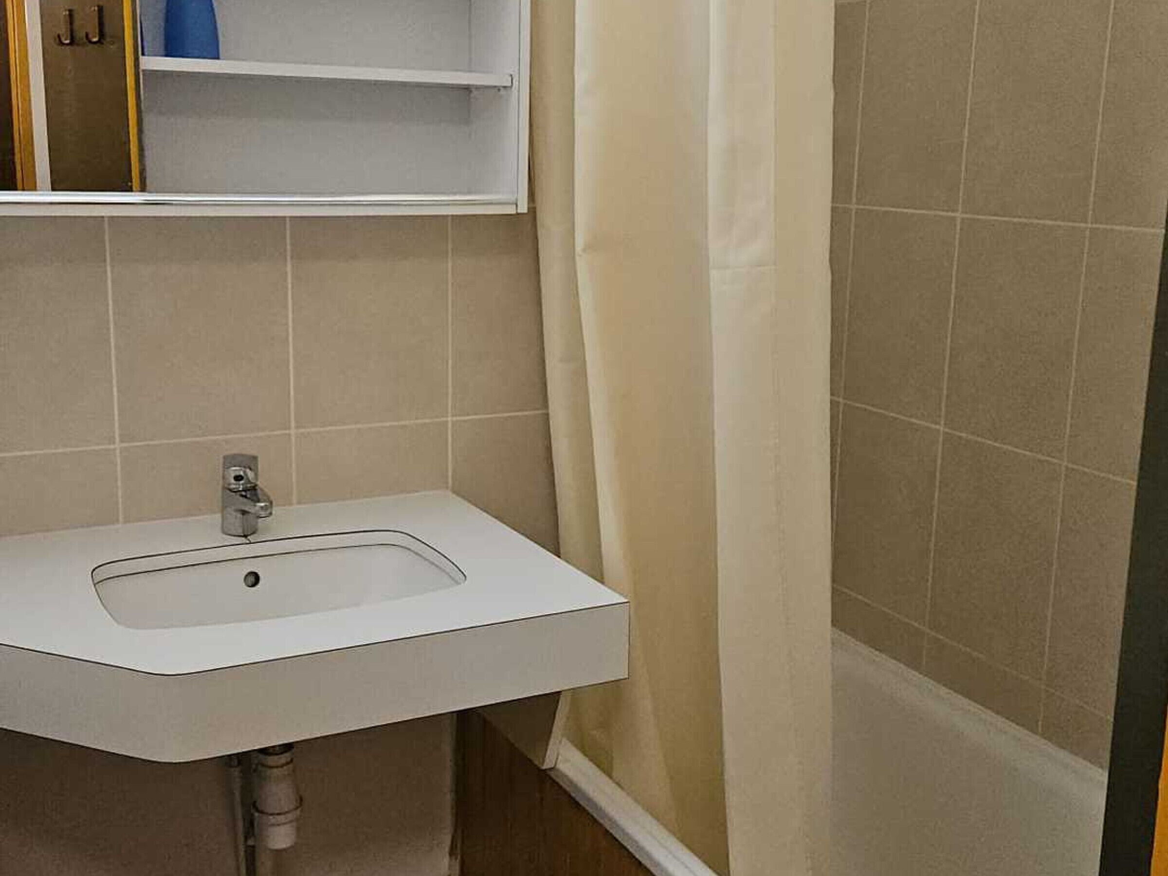 Ein Badezimmer mit einem weißen Waschbecken, einem Spiegel darüber und einer Duschvorhang.