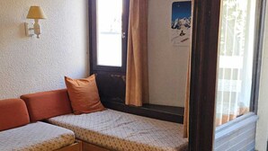 Una stanza piccola con un divano letto, un tavolo di legno e una finestra con tende.