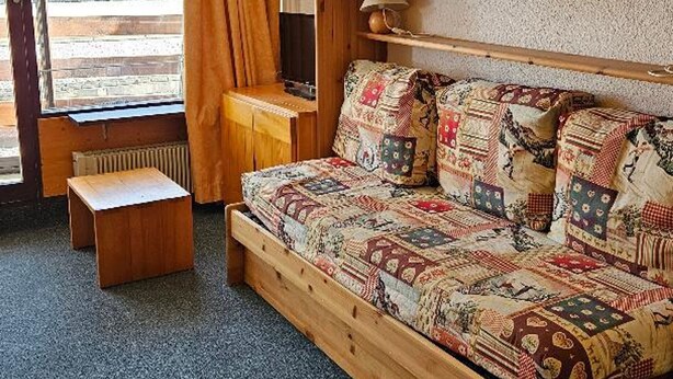 Una camera accogliente con un letto di legno, una piccola panca in legno e una finestra con tende.