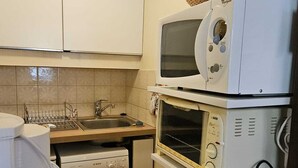 Una cucina compatta con lavastoviglie Bosch, un forno a microonde impilato e un lavello con scolapiatti.