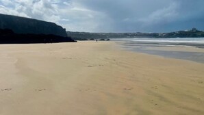 A beach with a wide sandy shore, a large cliff on the left, and a clear sky with scattered clouds. - Bramble Cottage a stunning detached cottage in the heart of St Columb Minor. (Newquay)