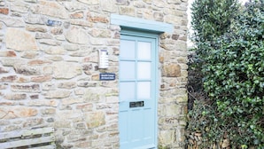 A stone building with a light blue door, a bench, and a sign indicating 'Bramble Cottage 20 Church Street'. - Bramble Cottage a stunning detached cottage in the heart of St Columb Minor. (Newquay)